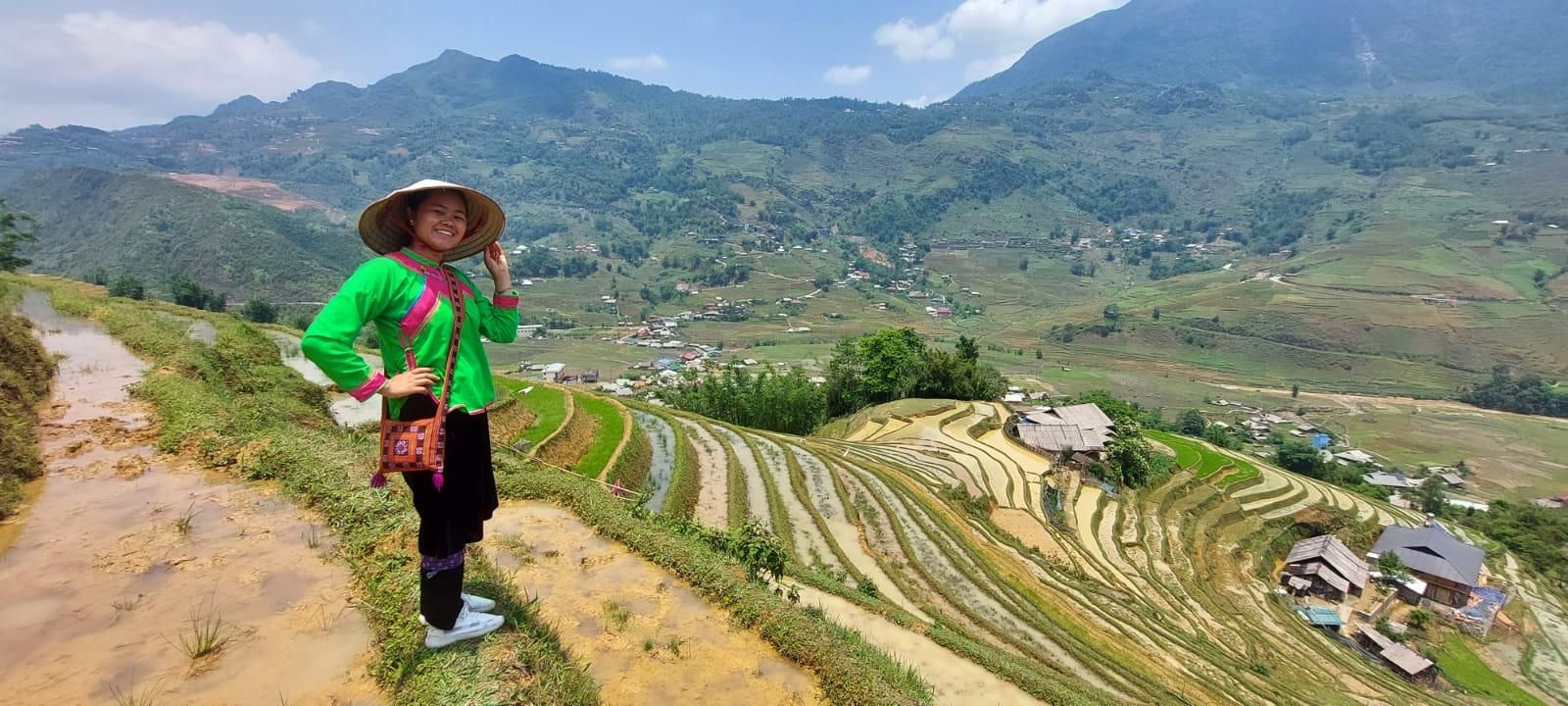 May, in a bright green traditional top and conical hat, on a rice terrace path above the valley