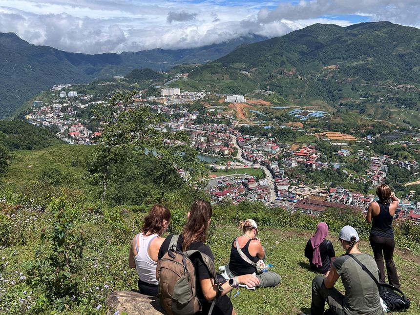 Hikers resting on a grassy hilltop above Sa Pa town and the green mountains