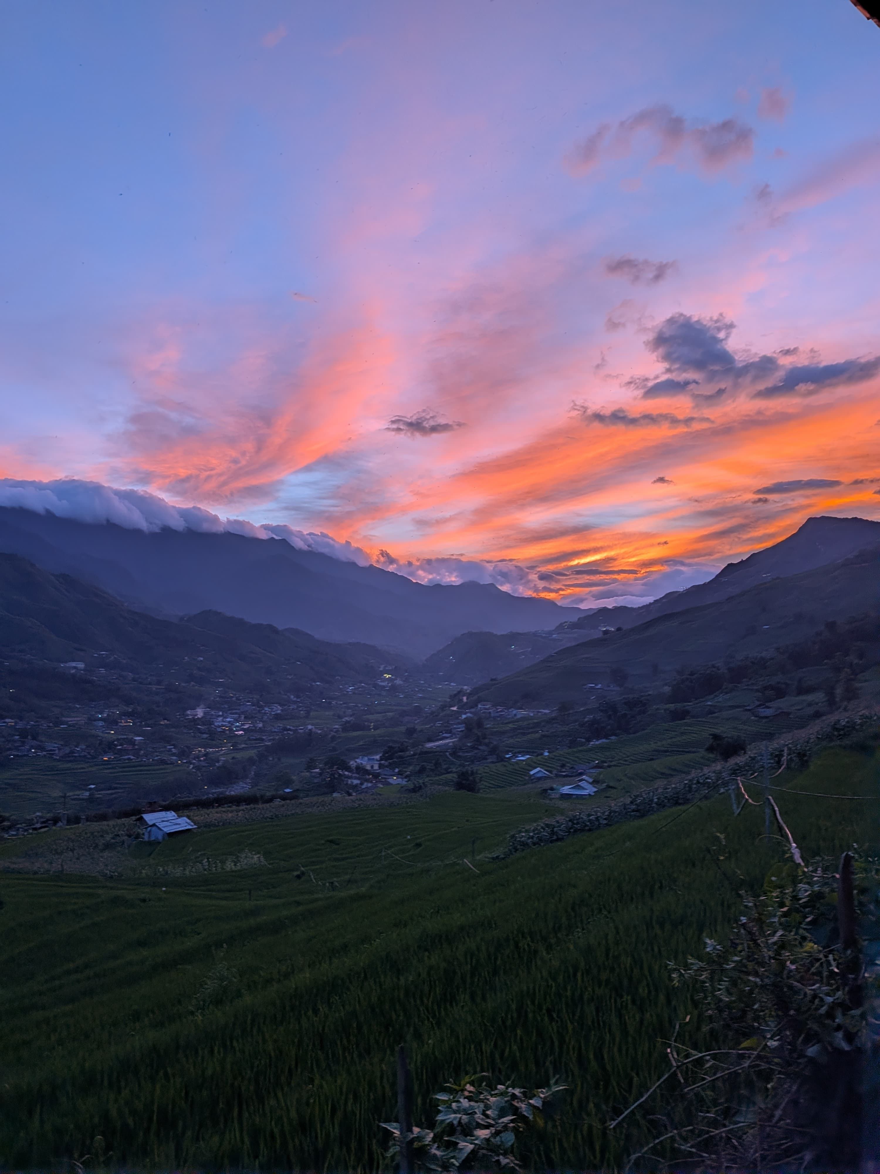 Pink and orange sunset clouds over a mountain valley and rice fields